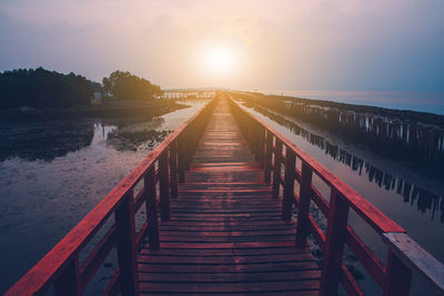 View of wooden footbridge over sea during sunset