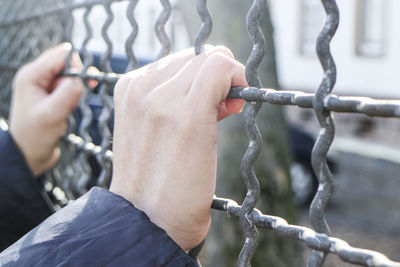 Cropped hands of person holding chainlink fence