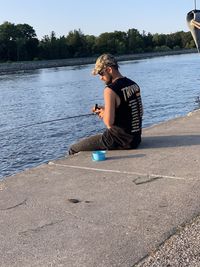 Man sitting on pier by lake against sky