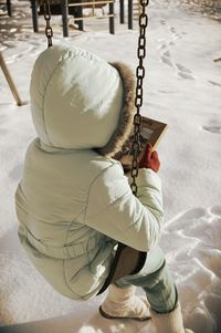 Full length of child holding picture frame while sitting on swing during winter