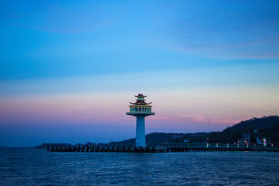 Lighthouse by sea against sky during sunset