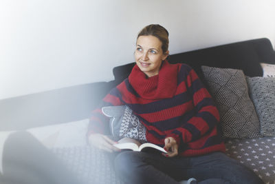 High angle view of woman with book sitting on sofa at home