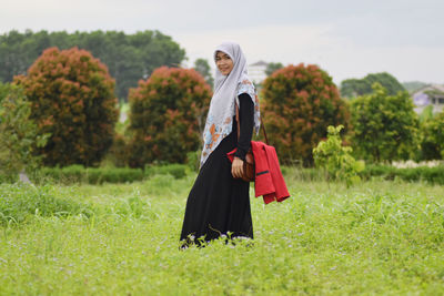 Portrait of smiling woman in hijab standing on field 