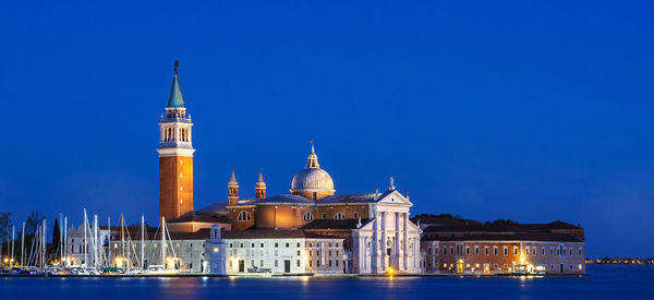 Illuminated st marks square by canal against clear blue sky