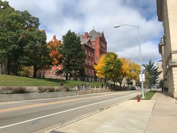 Road by trees and buildings in city against sky