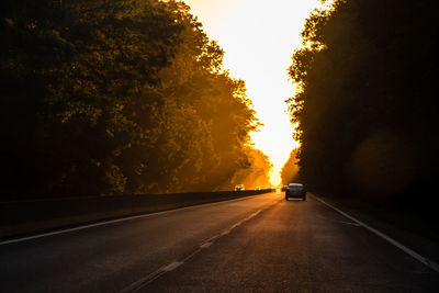 Road amidst trees against sky during sunset