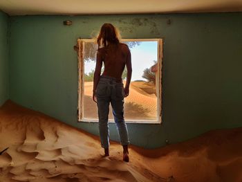 Rear view of topless woman standing on sand in abandoned room