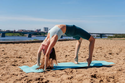 Middle aged woman in sportswear doing backbend yoga exercise on beach outdoor. wheel asana