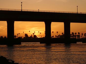 Silhouette bridge over sea against sky during sunset