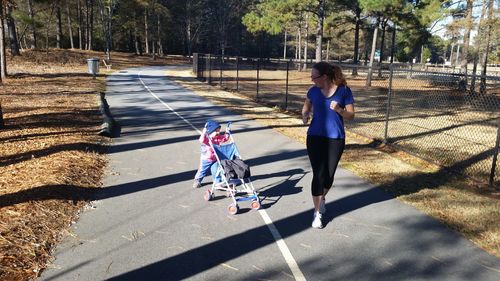 Full length of mother looking at child pushing baby stroller on road
