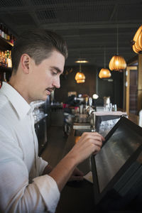 Side view of owner using cash register at checkout in restaurant