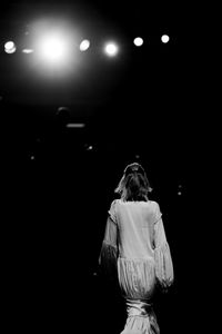 Rear view of woman standing against illuminated lights at night