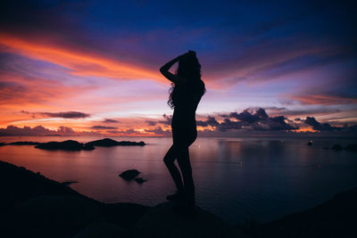 Silhouette man standing on rock against sea during sunset