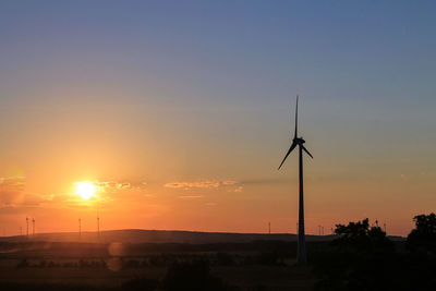 Silhouette windmill on landscape against sky during sunset