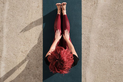 From above top view of anonymous barefooted woman in sportswear sitting resting after yoga exercise on mat on the street