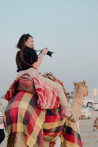 Young woman with camera sitting on camel