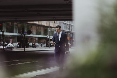 Businessman with bag using smart phone while walking in city