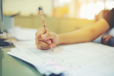 Cropped hand of woman writing in paper at classroom