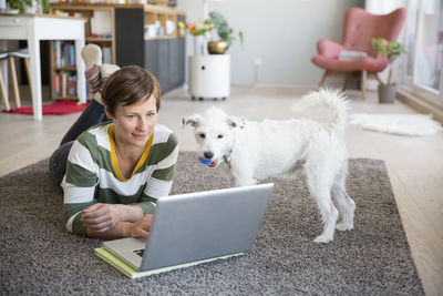 Woman lying on the floor in her apartement looking at laptop