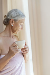 Senior woman wrapped in towel drinking cup of coffee in the morning