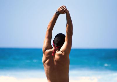 Rear view of shirtless man standing at beach against clear sky