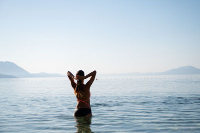 Rear view of woman standing in sea against clear sky