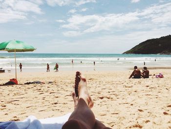 Low section of woman relaxing on beach against sky