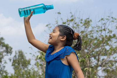 Side view of young woman drinking water against trees