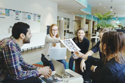 Businesswoman giving photographs to colleague during meeting in creative office