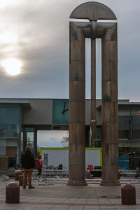 Rear view of man walking in city against cloudy sky