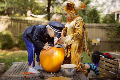 Brothers carving pumpkin on table at yard during halloween