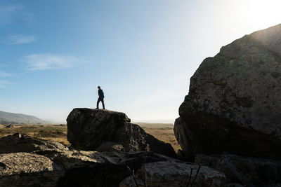 Lone person silhouetted against blue sky standing on large rock