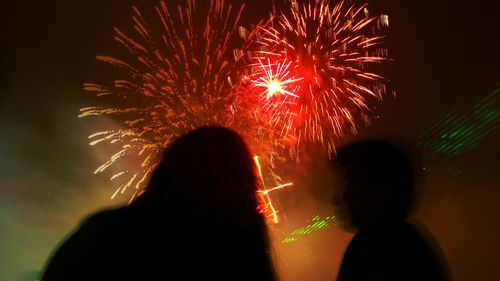 Low angle view of people against firework display at night