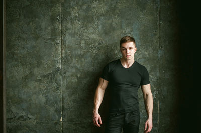 Portrait of muscular man standing by wall