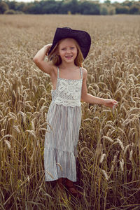 Girl in a black hat and a long dress stands in a field with spikelets of yellow wheat