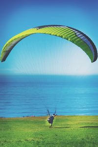 Person paragliding over sea against blue sky