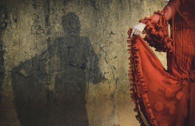 Shadow of woman dressed in flamenco dress on cracked wall, focus on wall shadow