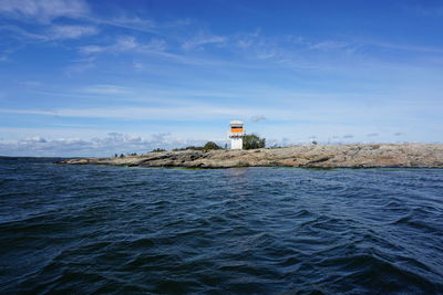 Lighthouse by sea against blue sky