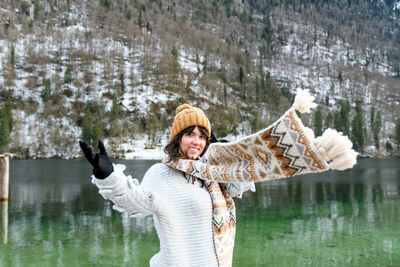 Young woman in winter sweater smiling, standing by a lake.
