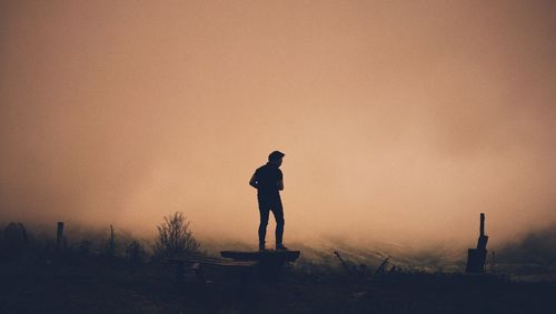 Silhouette man standing on field against sky during sunset