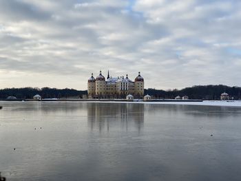 View of building by river against cloudy sky