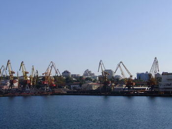 Cranes at harbor against clear blue sky