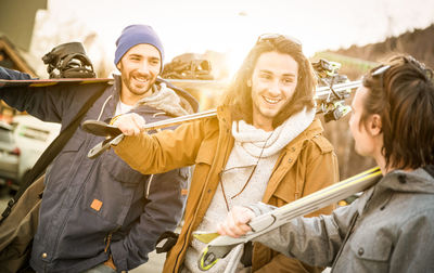 Friends holding ski equipment while standing outdoors