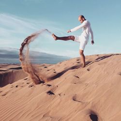 Woman standing on sand dune against sky