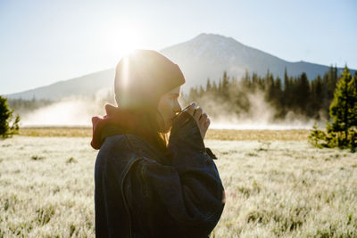 Young woman drinking coffee at sunrise near foggy mountain