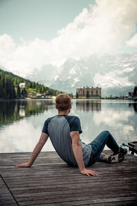 Rear view of man sitting on pier over lake against sky