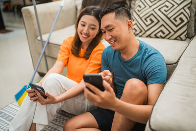 Young friends using mobile phone while sitting on sofa at home