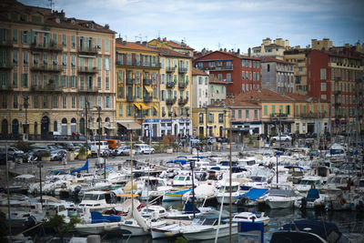 Boats moored by buildings in town against sky