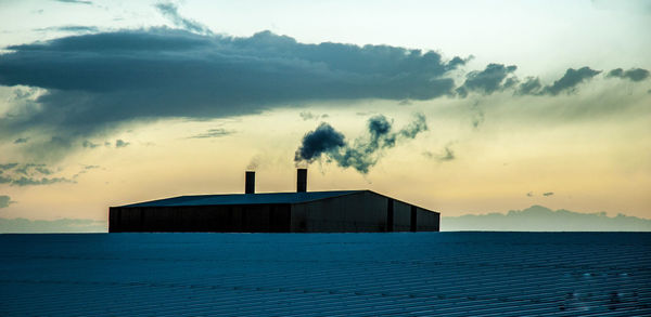 Silhouette building by sea against sky during sunset