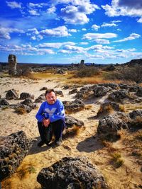 Man sitting on rock against sky